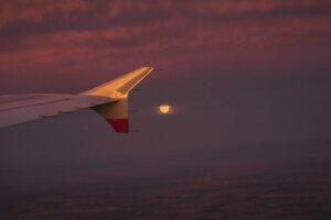 A view of the wing of an airplane with the moon in the distance