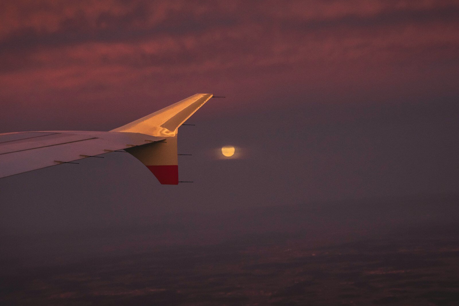 A view of the wing of an airplane with the moon in the distance